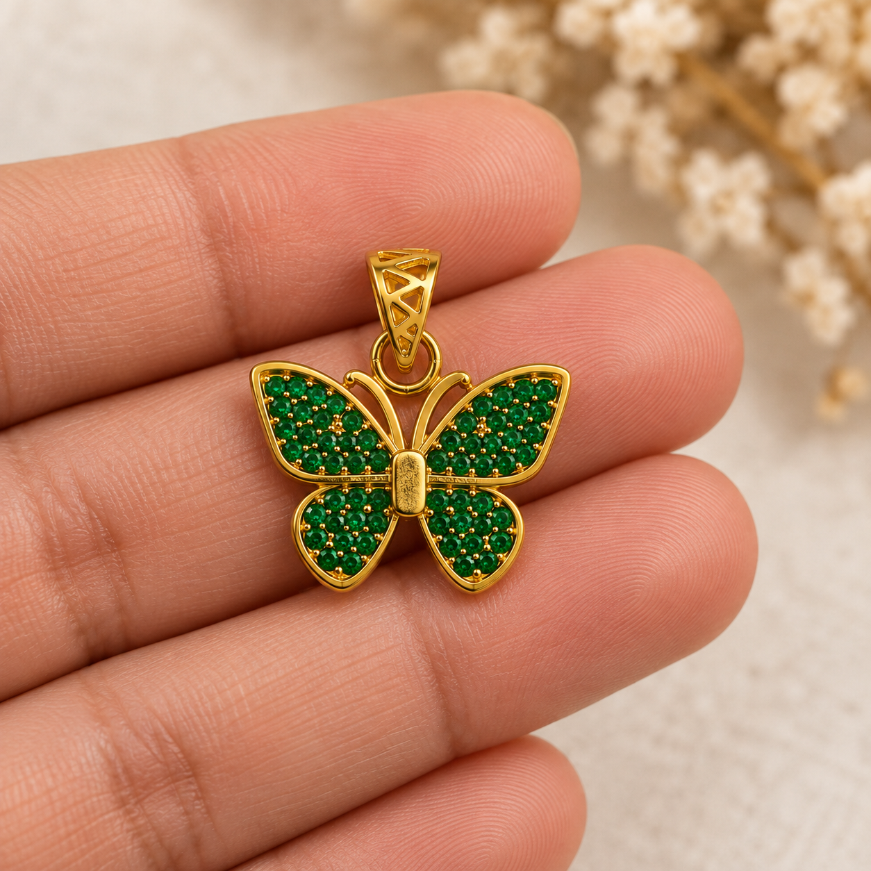 Emerald-green and gold butterfly pendant held between fingers to show its size and detail