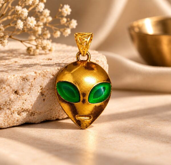 Astra Enigma gold alien pendant with green eyes displayed beside cream stone and white flowers