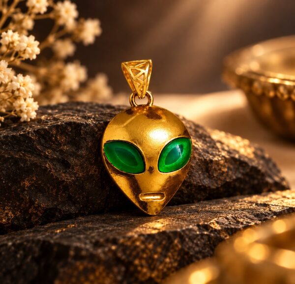 Astra Enigma gold alien pendant with vivid green eyes displayed on dark textured stone in warm evening light