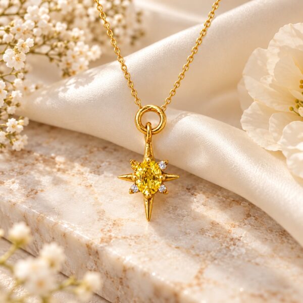 Solara gold starburst pendant with yellow stone styled on a chain beside ivory flowers and satin