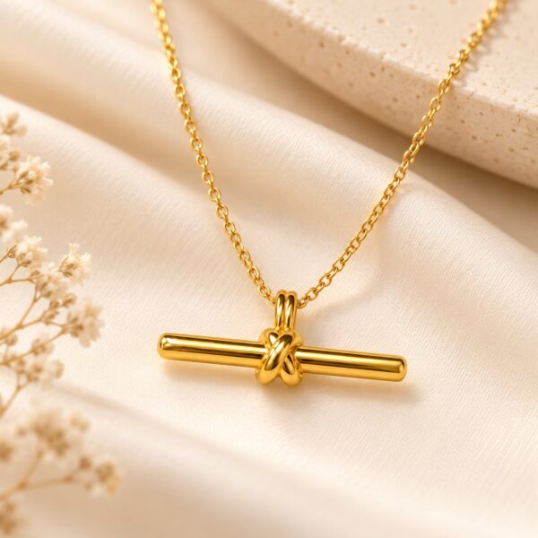 Gold-tone Aurelia Knot Bar Pendant displayed on a fine chain over soft ivory satin
