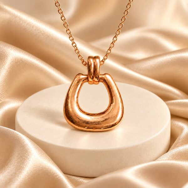 Seraphine rose-gold loop pendant displayed on a cream pedestal with satin and a fine chain