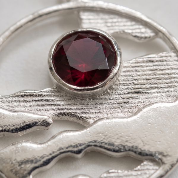 Close-up of bezel-set Ruby Red CZ and textured sterling silver on the Horizon Solstice landscape pendant