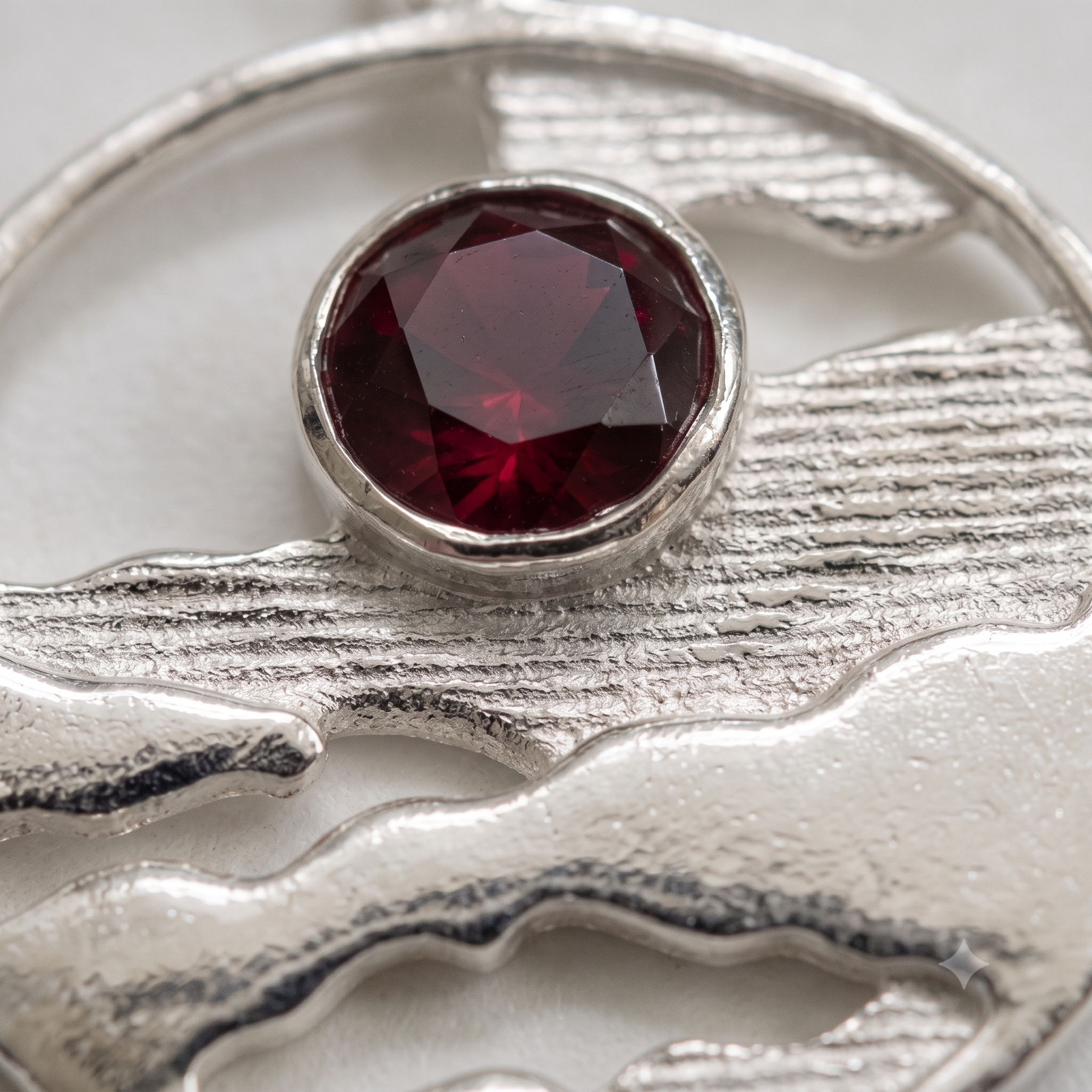 Close-up of bezel-set Ruby Red CZ and textured sterling silver on the Horizon Solstice landscape pendant