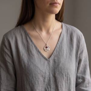 Woman wearing the Horizon Solstice Ruby Red CZ sterling silver landscape pendant necklace with a grey linen top