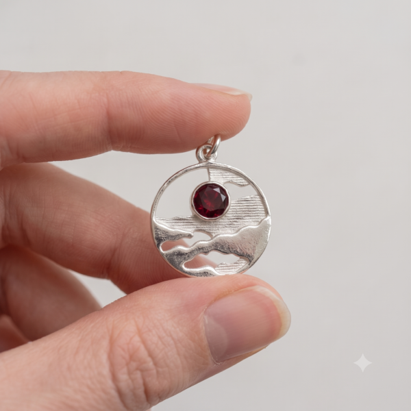 Horizon Solstice sterling silver landscape medallion with Ruby Red CZ shown held between fingers for scale