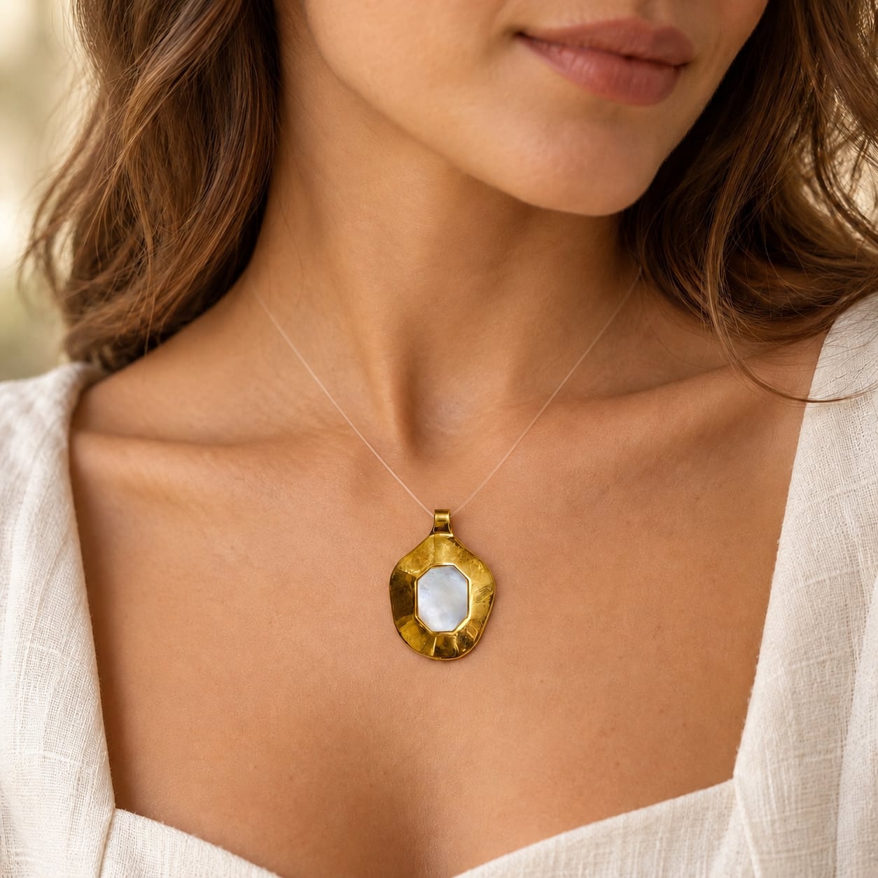 Woman wearing the Solis mother of pearl statement pendant in a warm gold finish with a white outfit.