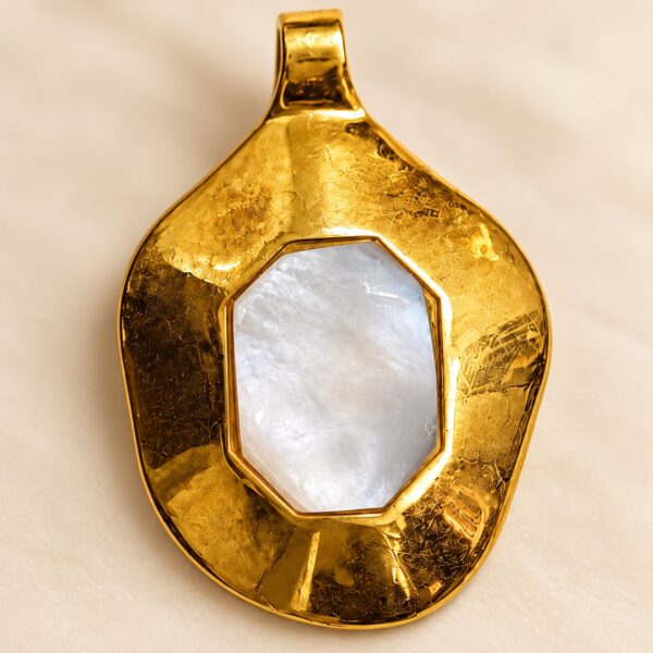 Close-up of Solis gold-tone statement pendant showing hammered texture and luminous mother-of-pearl centre.
