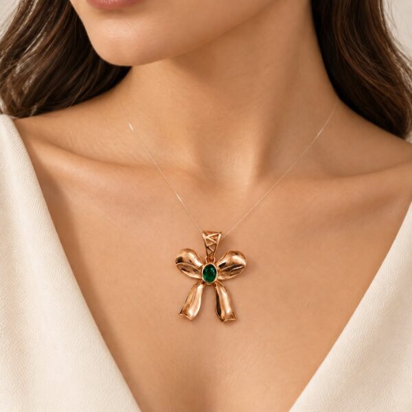 Woman wearing a rose-gold-tone ribbon bow pendant with an emerald-green CZ centre on a transparent nylon cord.